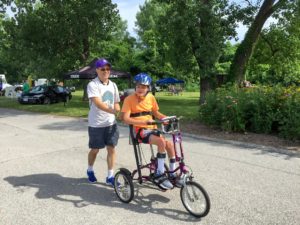 A young cyclist riding an adapted cycle with assistance from his father.