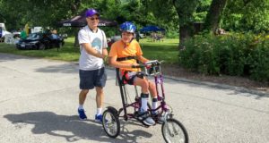 A young cyclist riding an adapted cycle with assistance from his father.