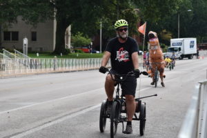Adult riding an adapted trike with his walking can in the rear basket.