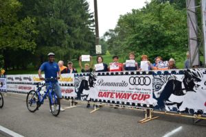 Shows a rider walking his bike past a group of friends who came out to support him. They're holding signs that say, "go Darius."